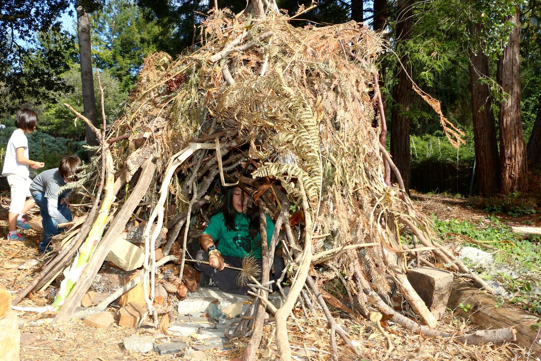 A child inside a hut made with branches and leavese