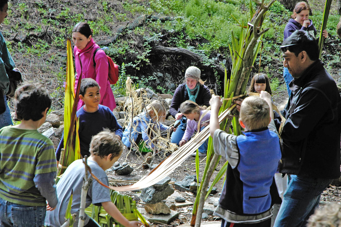  A group of 7 children and 3 adults making ephemeral sculptures with leaves, sticks, rocks and branches in a garden-based Create-with-Nature Zone