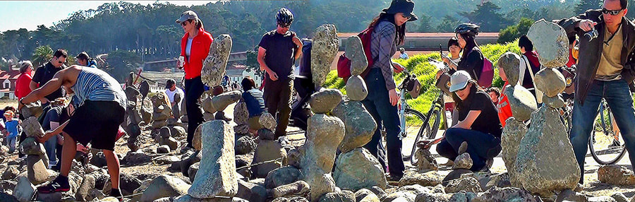 A crowd of about 15 people making and looking at balanced rock sculptures