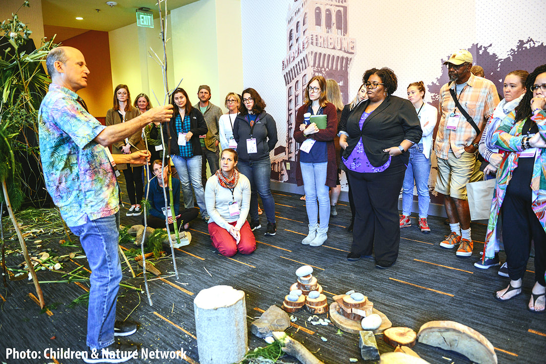 Zach Pine stands inside a Create-with-Nature Zone inside the Oakland Marriot Hotel, holding a dried fennel stalk, and speaking to a group of workshop particpants